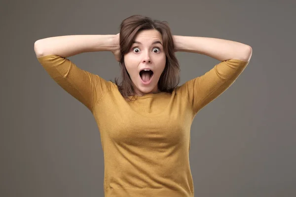 Shocked young woman with hands on head standing and shouting with surprise. — Stock Photo, Image