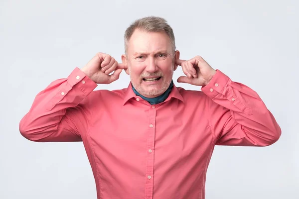Senior man in een rood shirt inpluggen oren met vingers — Stockfoto