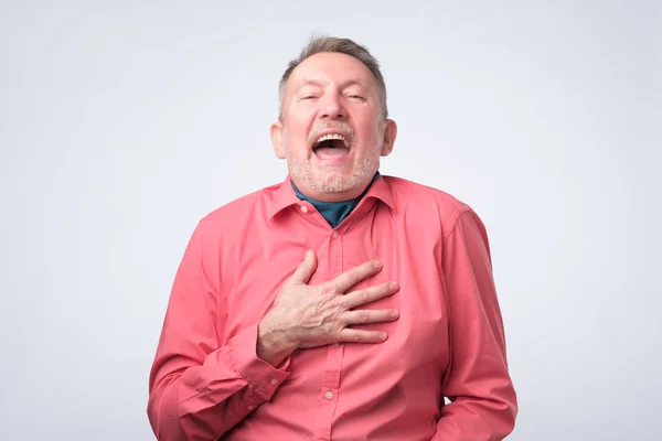 Senior im roten Hemd lacht und hält die Hand auf der Brust. — Stockfoto