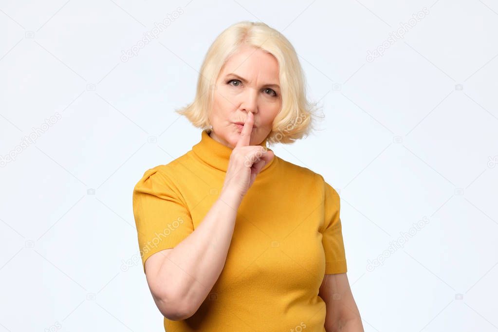 Old mature woman holding finger on lips mouth keep it in secret