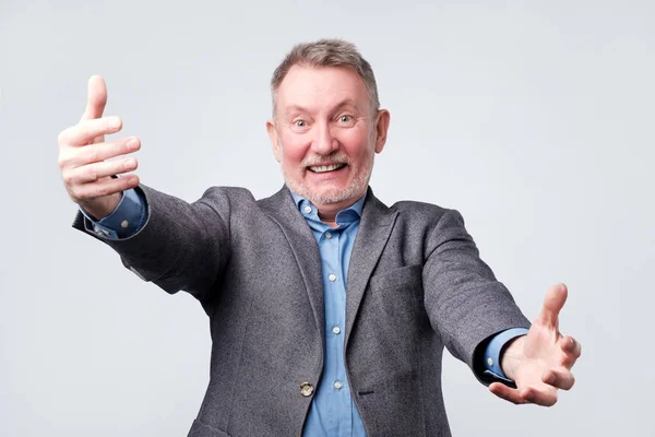 Hombre mayor con traje extiende alegremente las manos hacia adelante sobre un fondo blanco . — Foto de Stock