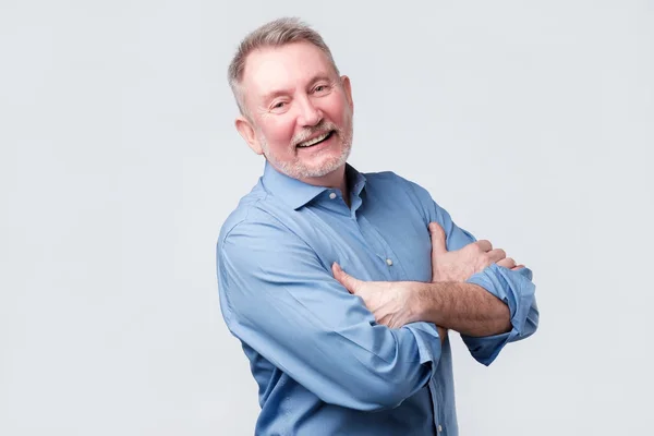 Viejo con la camisa azul cruzando los brazos, mirando hacia otro lado y sonriendo — Foto de Stock