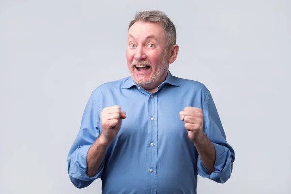 Homem sênior de camisa azul levantando punhos e sorrindo — Fotografia de Stock