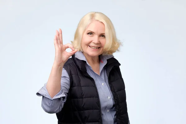Усміхнена старша блондинка леді жестикулює добре знак — стокове фото