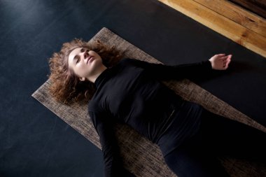 woman practicing in a yoga studio resting in shavasana or corps pose clipart