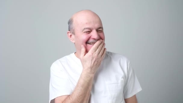 Starší plešatý muž pokrývající ústa a směje se. — Stock video