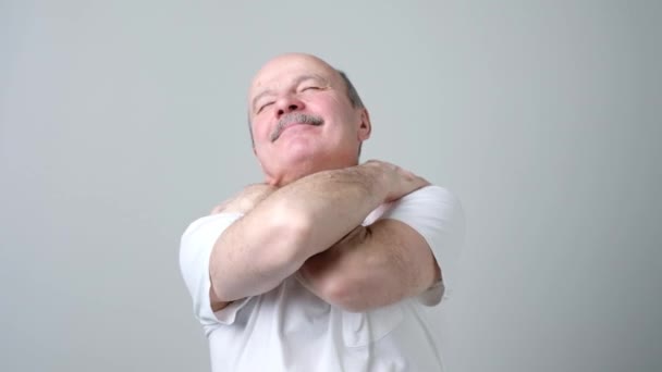 Hombre mayor cerrando los ojos y sonriendo de placer mientras se abraza — Vídeo de stock