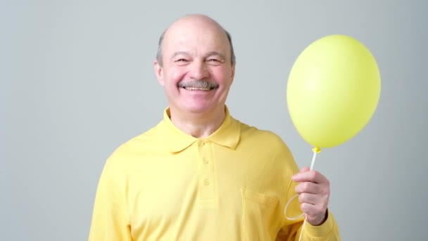 Senior man with yellow balloon with helium in hand — Stock Video