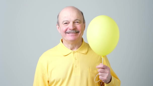 Senior man with yellow balloon with helium in hand — Stock Video