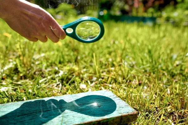 Man houdt een vergrootglas maken brand, gericht op hout. — Stockfoto