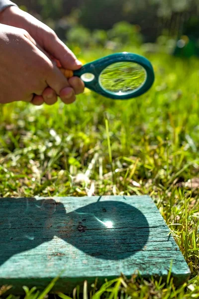 Man houdt een vergrootglas maken brand, gericht op hout. — Stockfoto