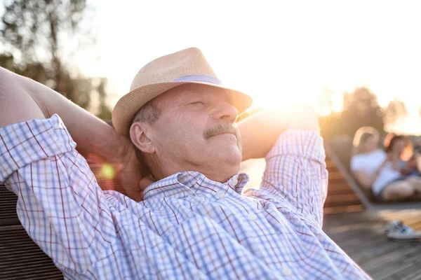 Старый латиноамериканец сидит на скамейке, улыбаясь, наслаждаясь летним солнечным днем . — стоковое фото