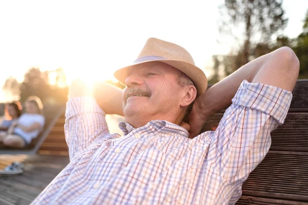 Oude Hispanic man zit op bankje, glimlachend, genieten van de zomer zonnige dag. — Stockfoto