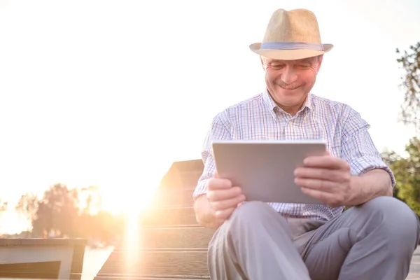 Homem sênior hispânico no chapéu de verão leitura tablet no espaço cópia do parque — Fotografia de Stock