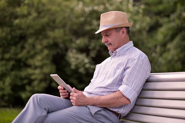 Homem sênior hispânico no chapéu de verão leitura tablet no espaço cópia do parque — Fotografia de Stock