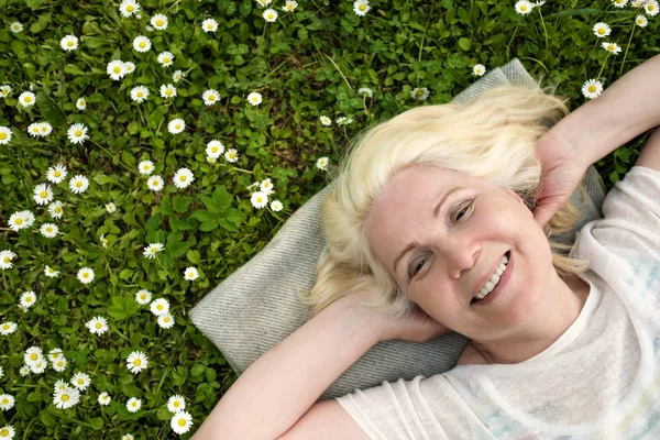 Mulher loira madura descansando no campo no prado verde com flores — Fotografia de Stock