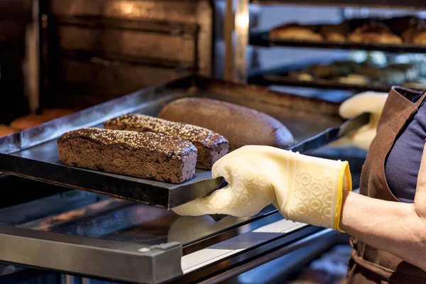 Padeiro segurando uma bandeja com pão fresco tirando-a do forno . — Fotografia de Stock