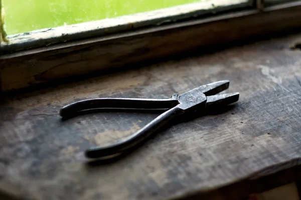 Old rusty plier on wooden shelf near window. — Stock Photo, Image