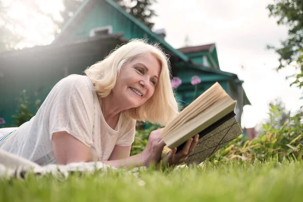 Europese volwassen blonde vrouw het lezen van een boek in de tuin. — Stockfoto