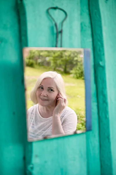 Приваблива старша блондинка дивиться на себе в дзеркало — стокове фото