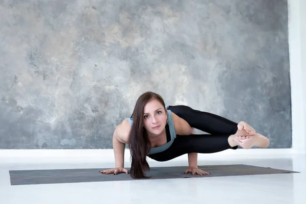 Young woman holding arm balance in Astavakrasana yoga pose