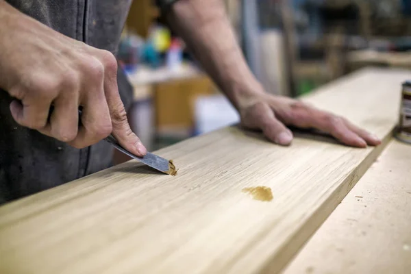 Knetmesser in der Hand des Mannes. Löcher aus einer Holzoberfläche entfernen. — Stockfoto