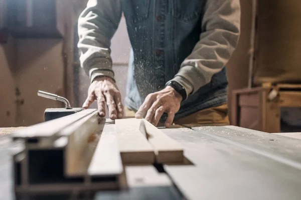 Sierra eléctrica cortando tabla de madera. Hombre trabajando en taller de carpintería — Foto de Stock