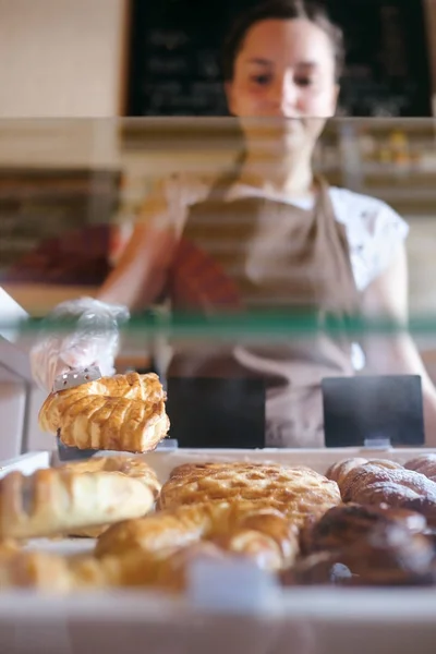 Trabajadora seleccionando magdalenas de un mostrador en una pequeña panadería —  Fotos de Stock