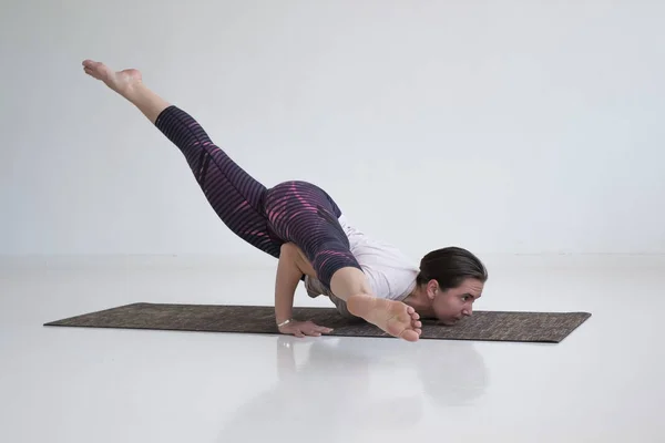 Mujer joven practica yoga asana Eka Pada Kaundiniasana 2 en la habitación blanca . — Foto de Stock