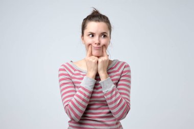 Kadın, parmaklarını ağzının kenarlarına uzatarak sahte gülümseme sergiliyor.