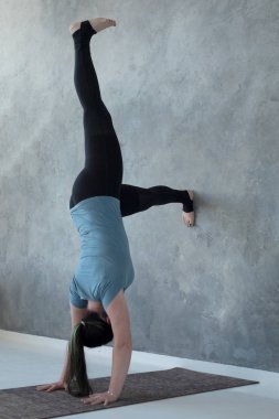 Duvara yakın ellerde durmayı öğrenen kadın. Baş aşağı yoga pozisyonu