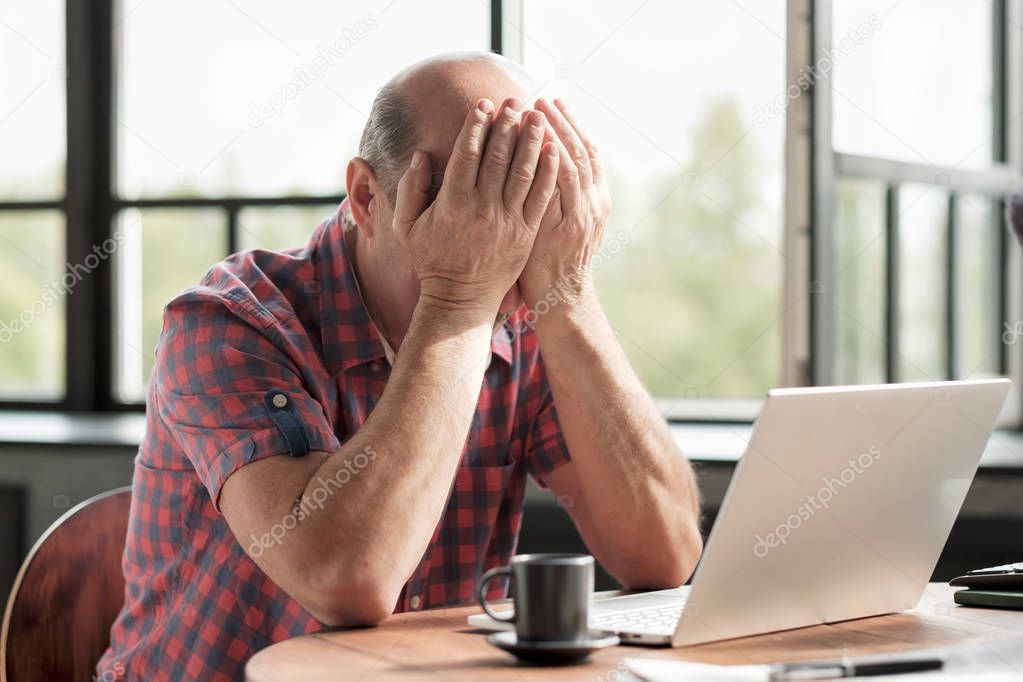 Man rubbing his tired eyes. He is tired to look on laptop screen