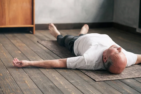 Мужчина медитирует на деревянном полу и лежит в позе Шавасаны после тренировки — стоковое фото