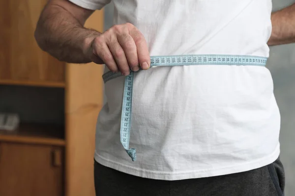 Мужчина измеряет живот измерительной лентой, стоящей в гостиной. . — стоковое фото