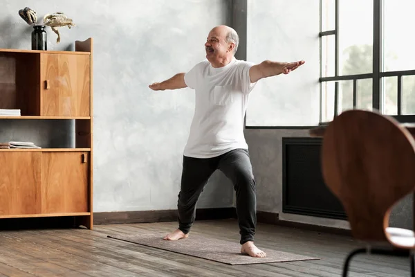 man standing in warrior two yoga pose practicing in living room
