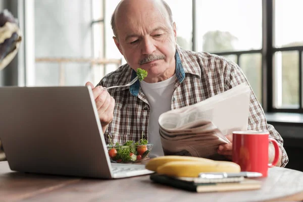 Homem tomando café da manhã saudável enquanto sentado na mesa da cozinha com laptop — Fotografia de Stock