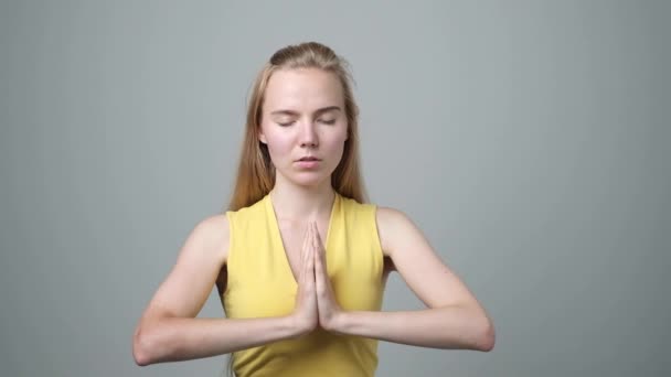 Girl standing in meditative pose against gray wall with closed eyes — Stock Video