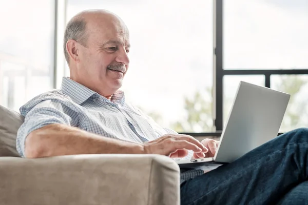 Seniror hispânico homem na sala de estar com laptop sorrindo — Fotografia de Stock