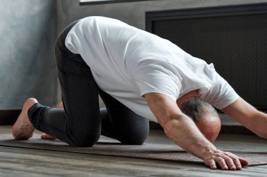 Evde yoga yapan ve uzun köpek pozu alan yaşlı adam