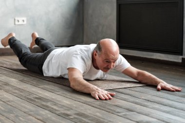 Kıdemli İspanyol adam egzersiz mat Üzerinde Shalabhasana yapıyor