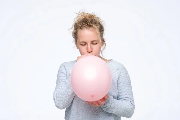 Kvinna i gblue sweateris blåser rosa ballong förbereder för födelsedagsfest — Stockfoto