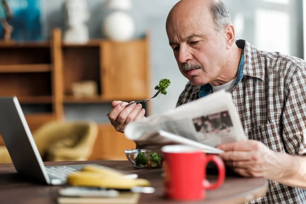 Старший латиноамериканец ест свежий салат утром, сидя в гостиной — стоковое фото