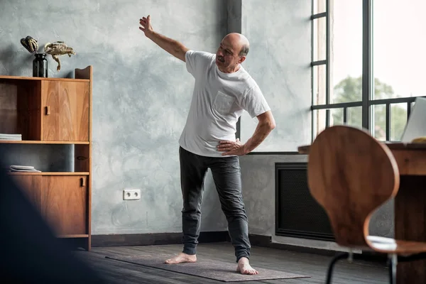 Ανώτερος άνθρωπος εξάσκηση γιόγκα τρικονάσανα ποζάρει στο σαλόνι — Φωτογραφία Αρχείου