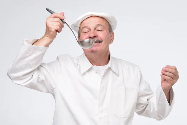 Male cook chef in white uniform tasting food from ladle — Stock Photo, Image