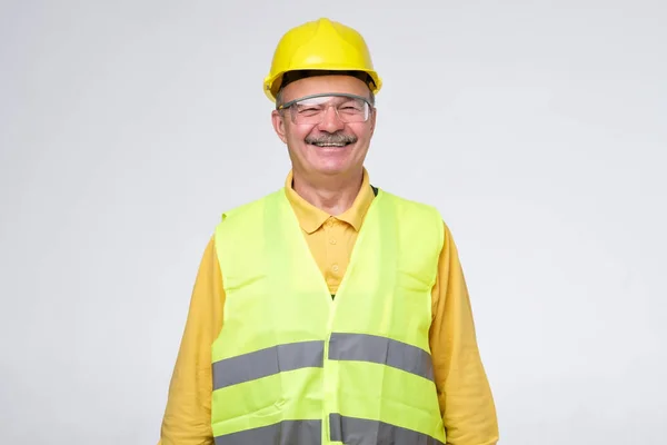 Trabajador de construcción hispano mayor en sombrero duro sonriendo sobre fondo gris . — Foto de Stock