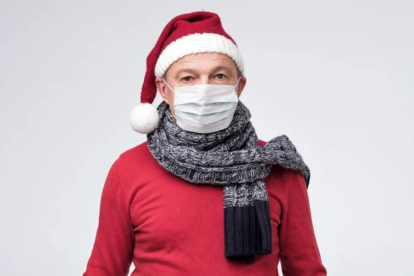 Pria bertopi Natal merah menutup wajah dengan topeng medis yang melindungi dari virus. — Stok Foto