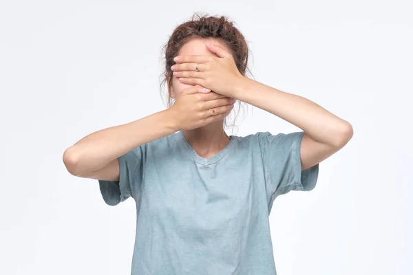 Ung kvinna i blå t-shirt som täcker ansikte med händer — Stockfoto