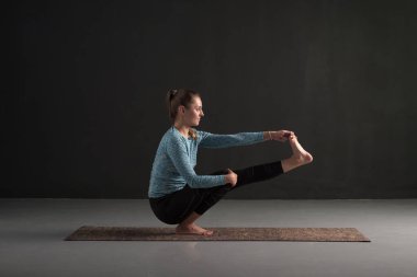 Yoga yapan genç ve güzel bir kadın tek bacağıyla dengede duruyor..