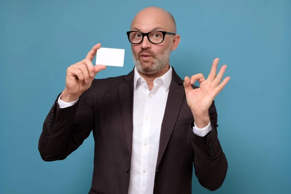 Όμορφος φαλακρός επιχειρηματίας με γενειάδα κρατώντας πιστωτική κάρτα κάνει εντάξει σημάδι — Φωτογραφία Αρχείου