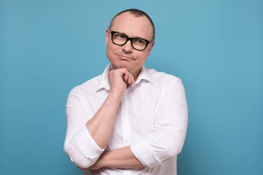 Beyaz gömlekli bir işçi şüphe ve güvensizlikle dolu bir stüdyoda poz veriyor..